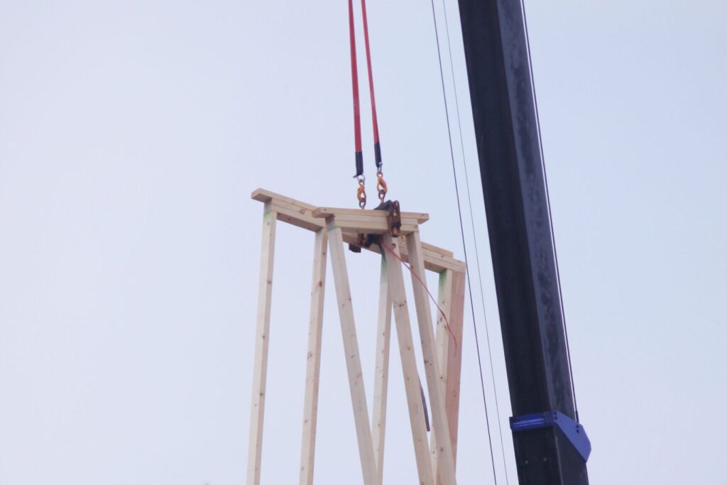 クレーンで吊り上げた木のパネルを組み上げる建て方の現場