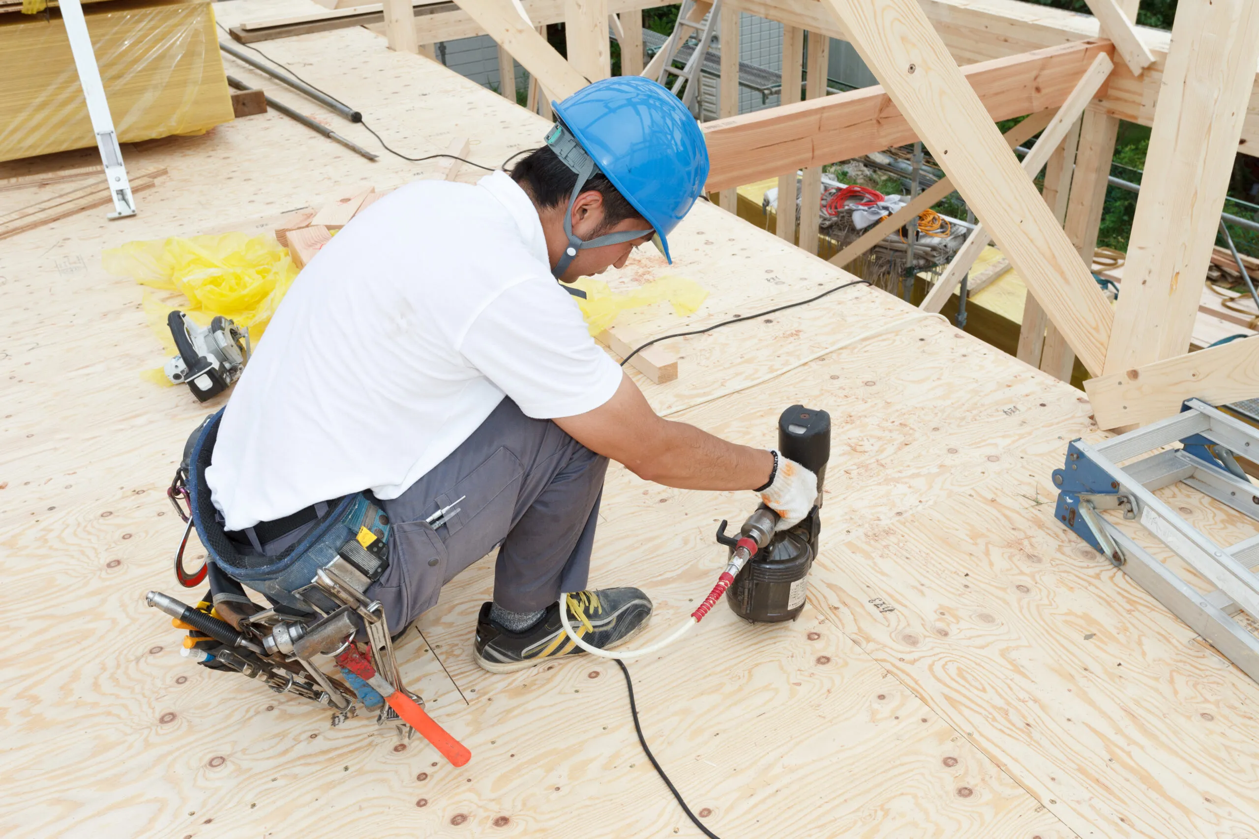 上棟後、木造の小屋組の上で屋根下地を釘打ちで留めていく現場の作業