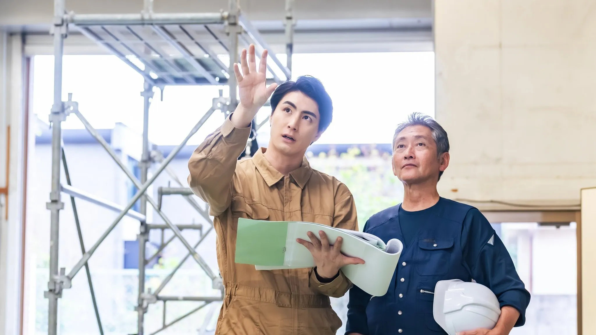 建築中の現場で図面を手に説明する棟梁と現場監督